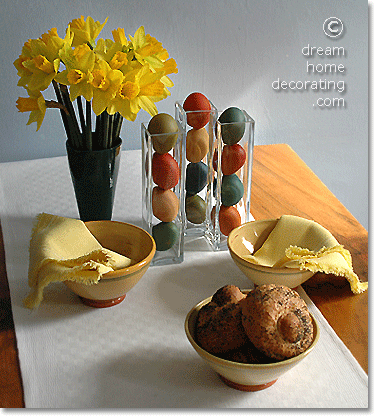 Hand-dyed Easter eggs in narrow glass vases on a yellow/white Easter table