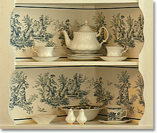 toile wallpaper on the back of an open cupboard, with staffordshire transferware