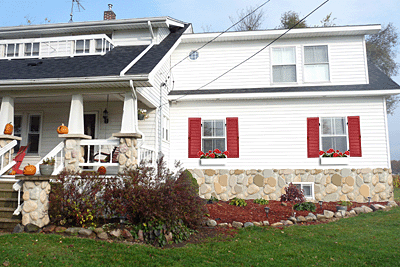 House with white cladding, windowboxes and red exterior wood shutters